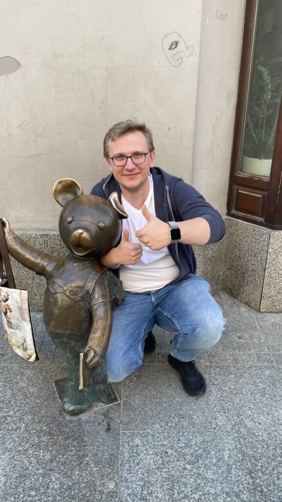 Zdjęcie przedstawia Jakuba Kowalewskiego klęczącego przy złotym pomniku Misia Uszatka.